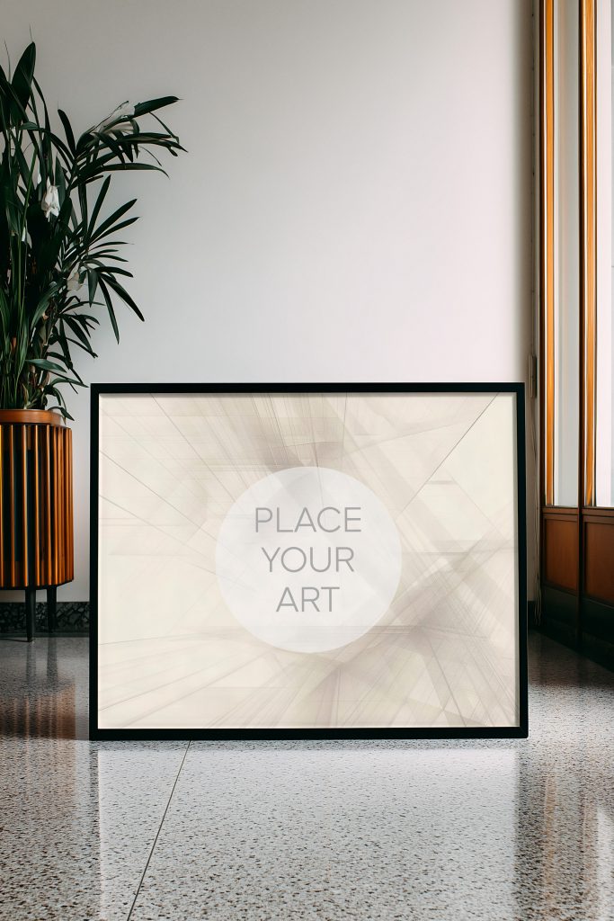 Large horizontal black wall art frame mockup on a polished terrazzo floor next to a vintage wooden planter with a lush green plant in a bright mid-century room.