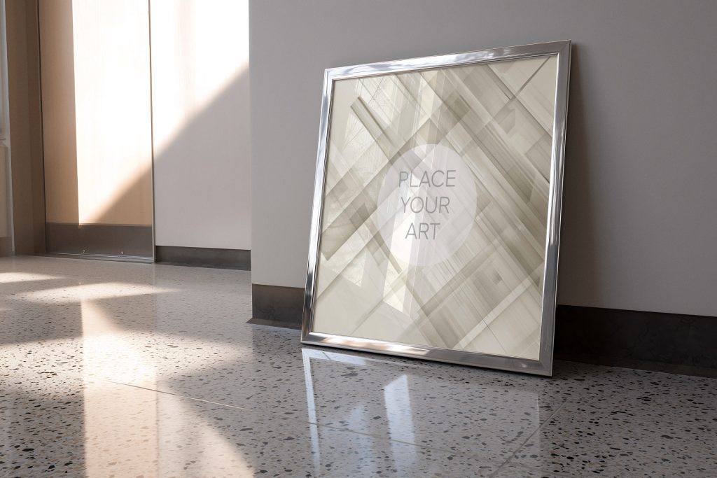 wall-art-frame-mockup-atomic-era-retro-chrome-terrazzo-floor.jpg Square wall art frame mockup with a polished chrome finish leaning against a neutral wall on a reflective terrazzo floor in a bright retro interior.