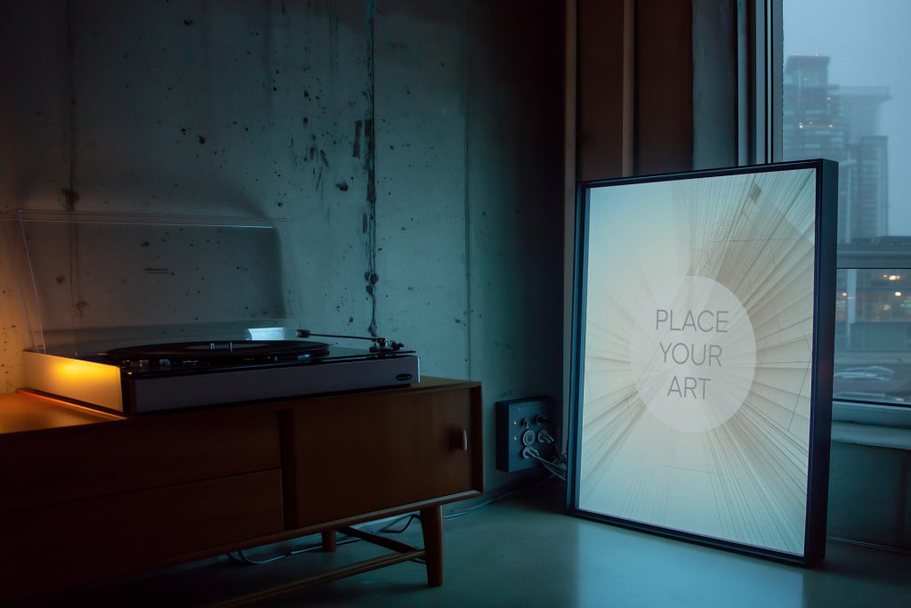 Lo-Fi interior with a vertical wall art frame on the floor, vintage turntable on a wooden cabinet, and rainy city window view.