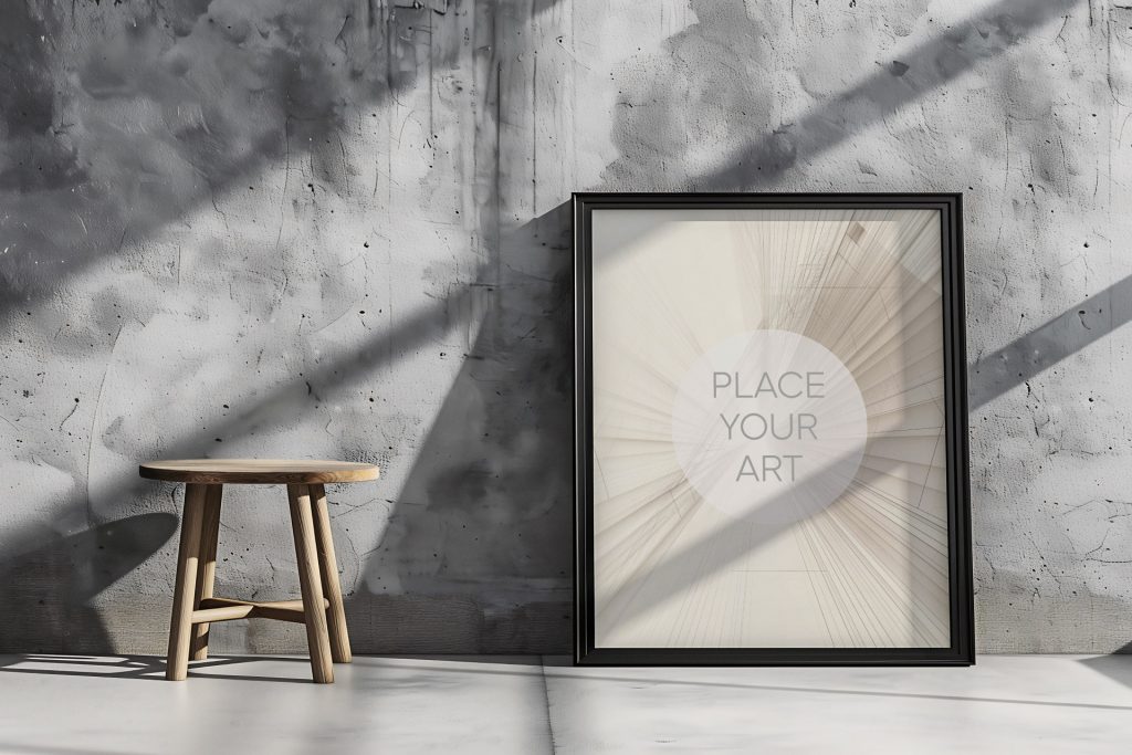 Vertical poster mockup leaning on a concrete studio floor next to a minimalist round wooden stool against a weathered raw cement wall with harsh sunlight shadows.